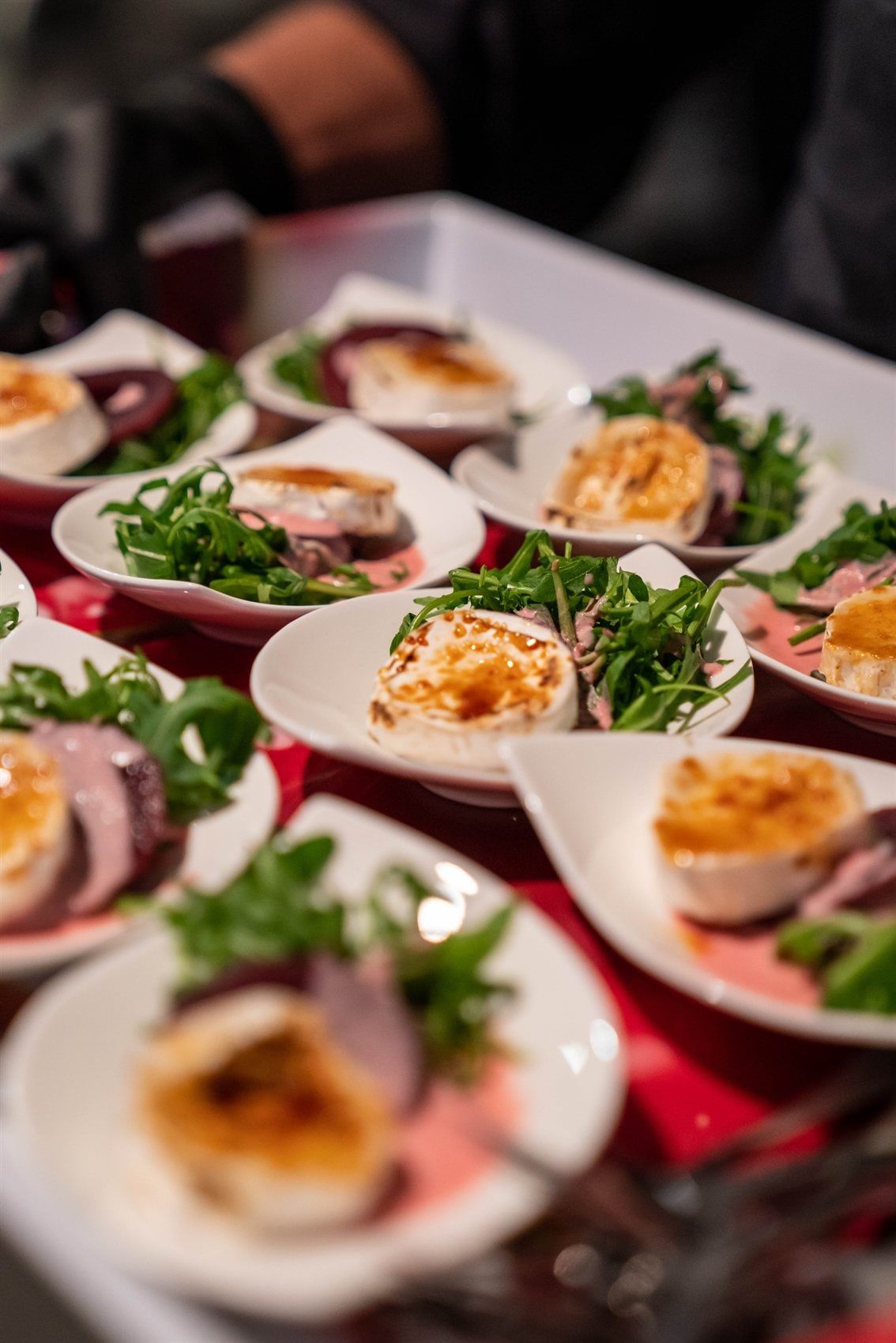 Reihen von Vorspeisen mit Rucola, Roastbeef und gratiniertem Ziegenkäse auf weißen Schälchen