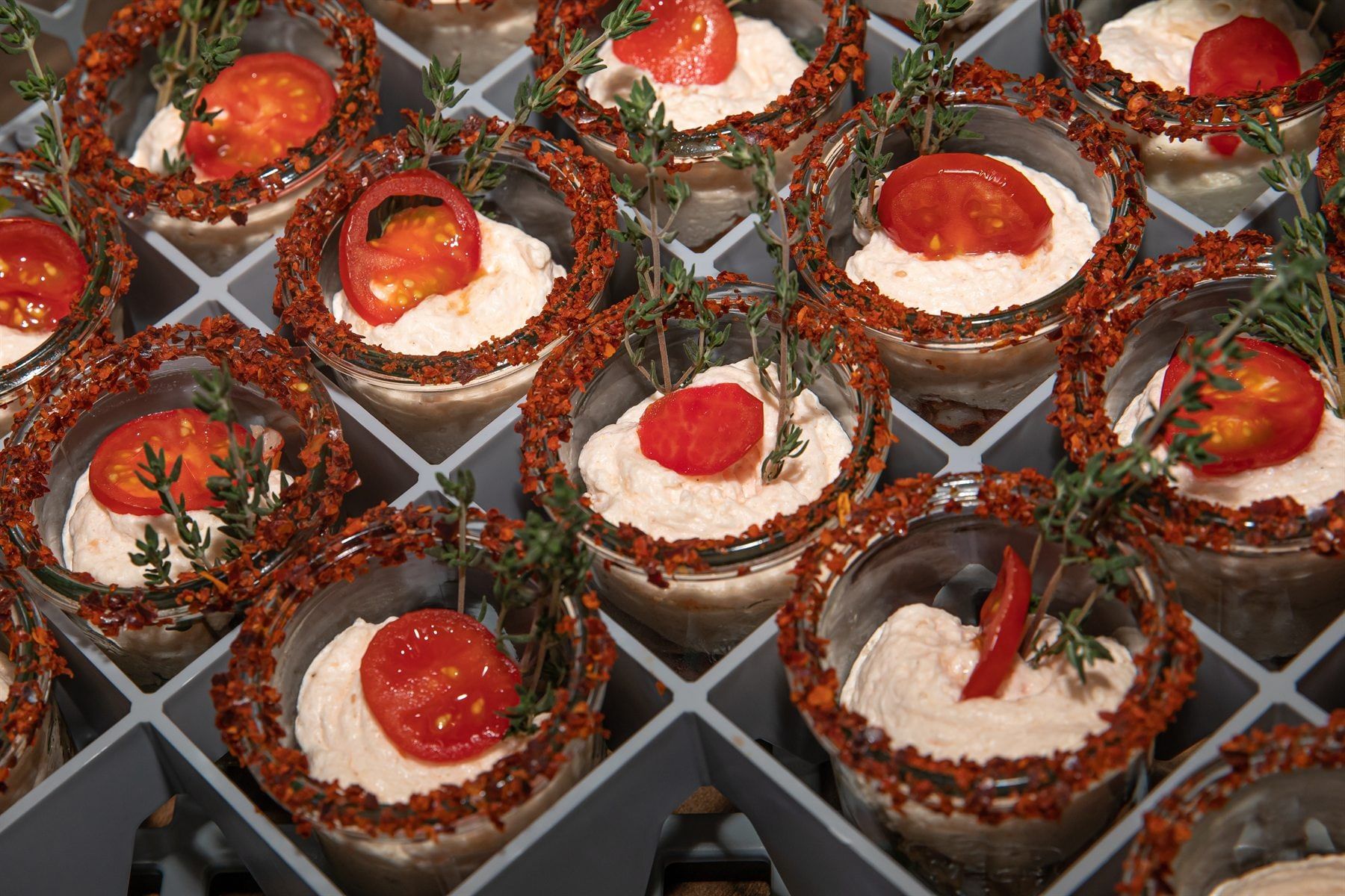 Kleine Gläser mit heller Creme und Tomate, dicht an dicht auf einem Tablett angerichtet
