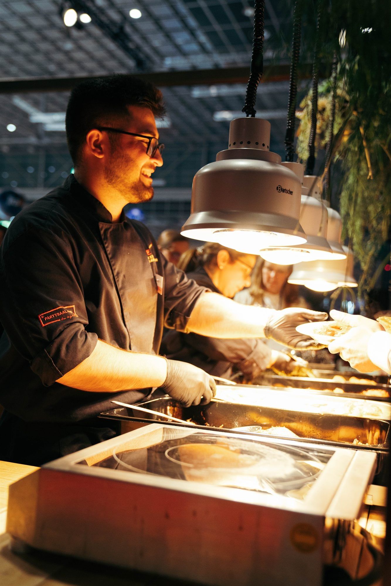 Koch von METZ. richtet unter warmen Wärmelampen Teller an einer Live-Cooking-Station an