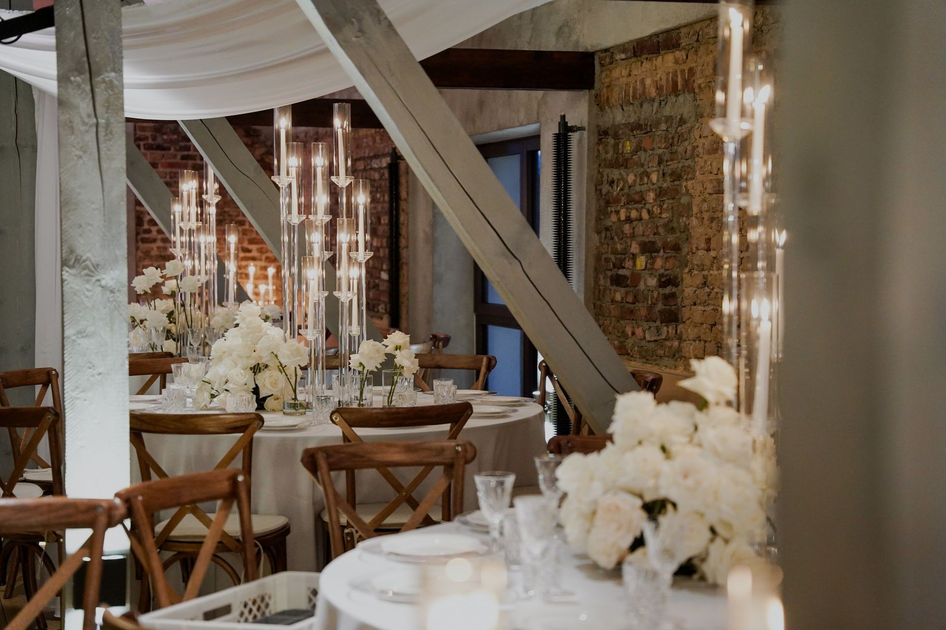 Runde Festtafeln mit weißen Rosen, Kristallgläsern und hohen Glaskandelabern im Festsaal des Andreashauses, dahinter Holzstützen und Backsteinwand