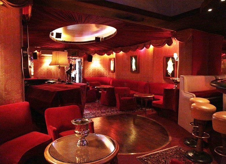 Lounge im Erdgeschoss der Kokett Bar mit roten Samtsesseln, runder Parkettfläche, Stehlampe und beleuchteter Deckenkuppel