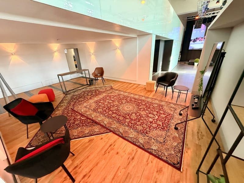 Eine ausgefahrene Lounge-Box mit Orientteppich, Sesseln und Holzboden am Rand der Bauwerk-Halle