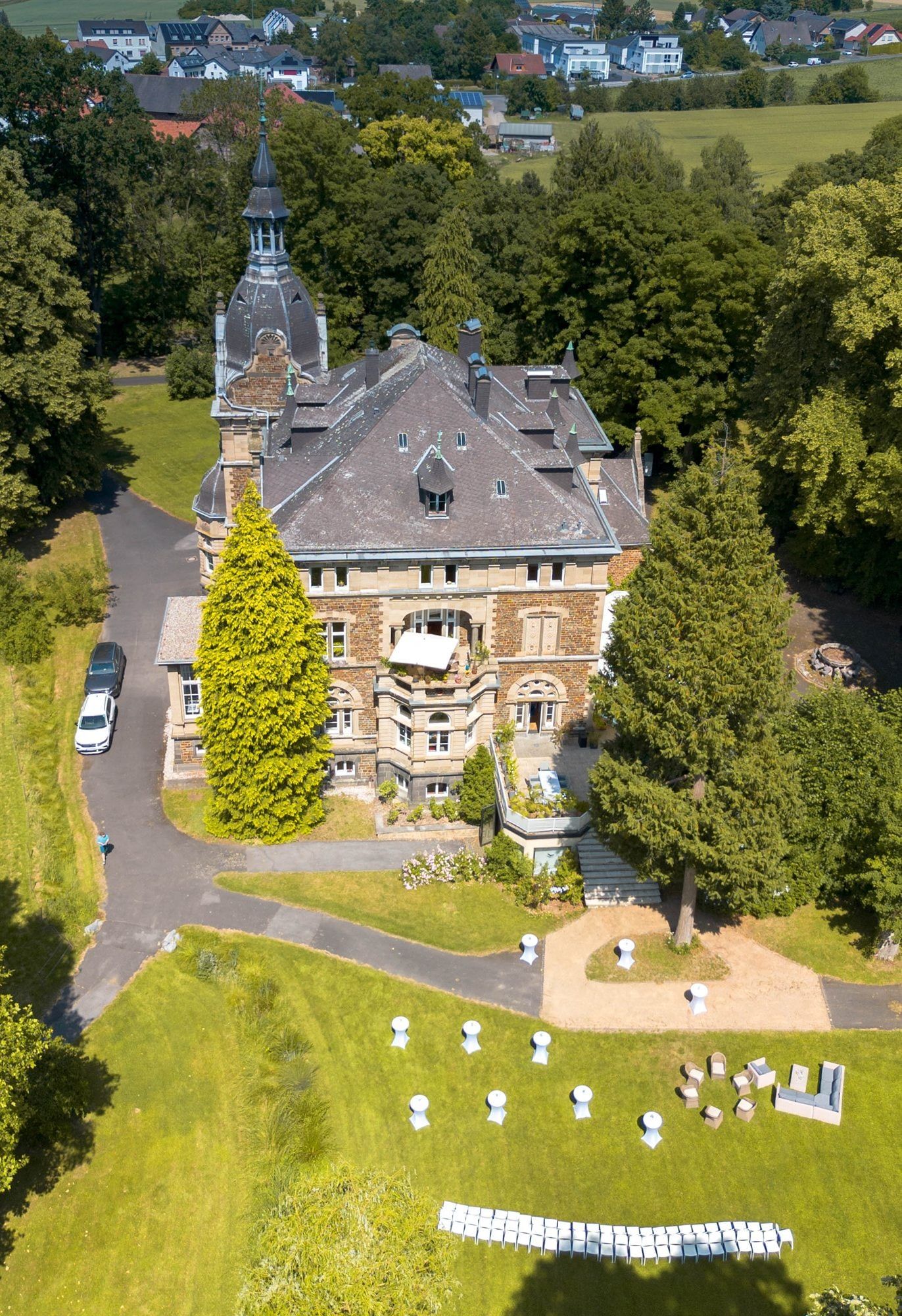 Blick von oben auf das Schloss, davor der Park mit Stehtischen, Lounge und Stuhlreihen für eine freie Trauung