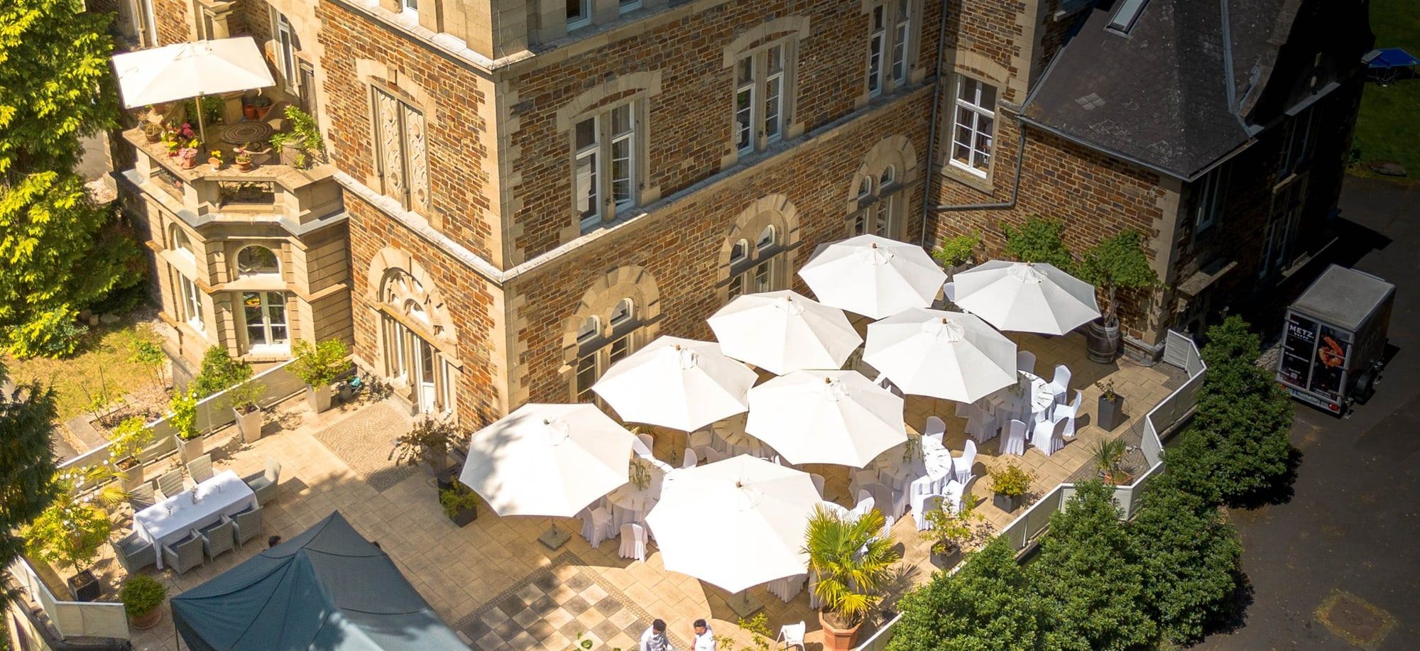 Die Terrasse von Schloss Vettelhoven aus der Luft, mit weißen Sonnenschirmen über festlich eingedeckten Tischen