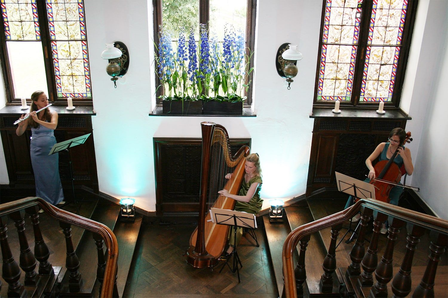Musikerinnen mit Harfe, Querflöte und Cello im Treppenhaus von Schloss Wachendorf zwischen geschnitzten Holzgeländern