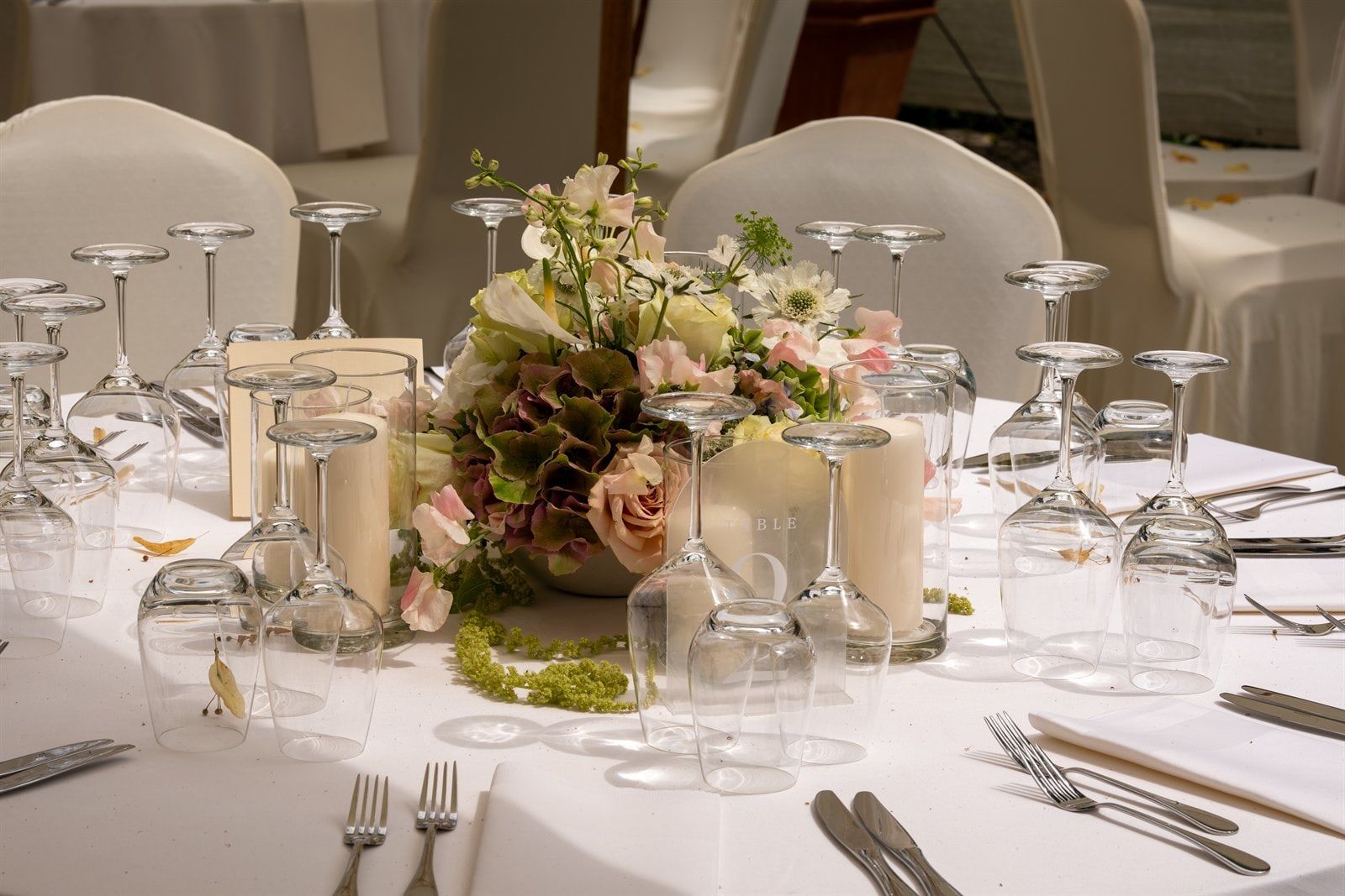 Tischgesteck aus Hortensien, Rosen und Wicken zwischen Kerzen und Gläsern auf einer Hochzeitstafel