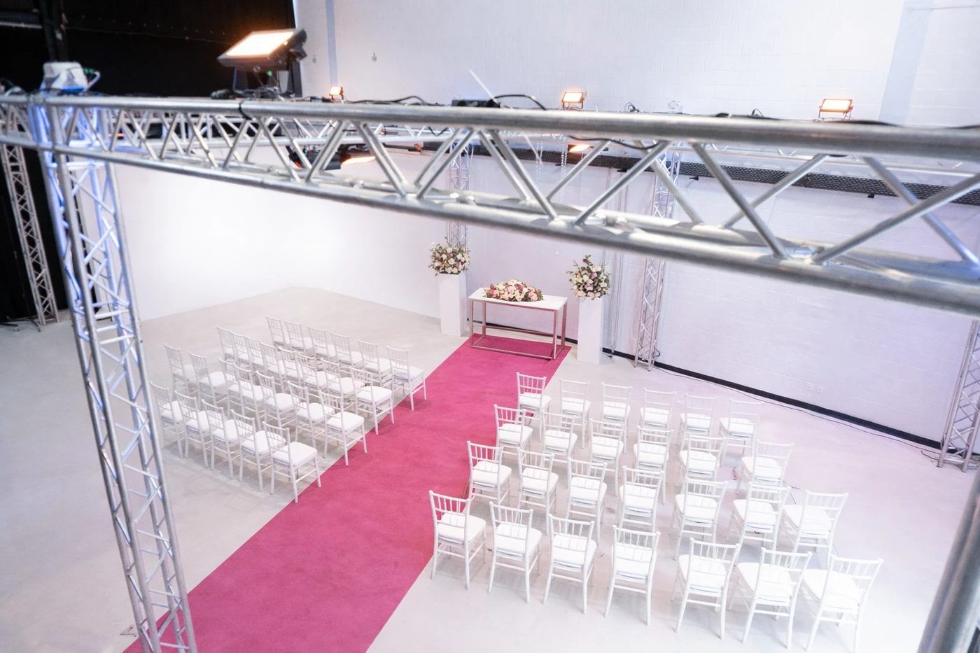 Trauung im Bauwerk Studio Köln von oben, weiße Stuhlreihen an einem pinken Teppich und ein Blumentisch vor der weißen Wand