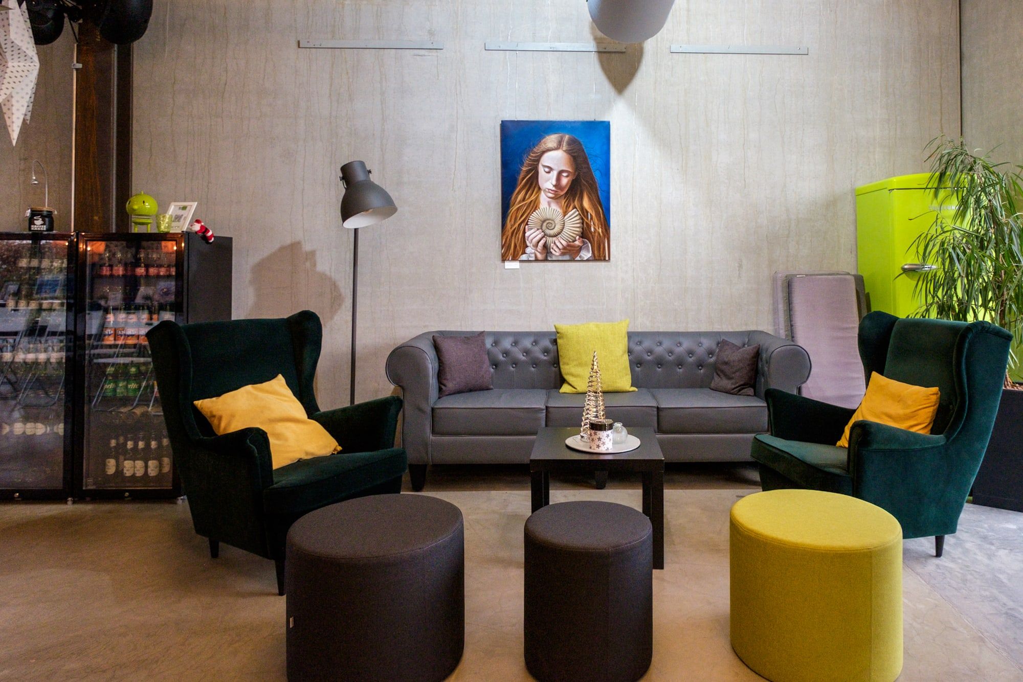 Lounge im BRÜNEO mit Chesterfield-Sofa, grünen Ohrensesseln, gelben Hockern und einem Gemälde an der Betonwand