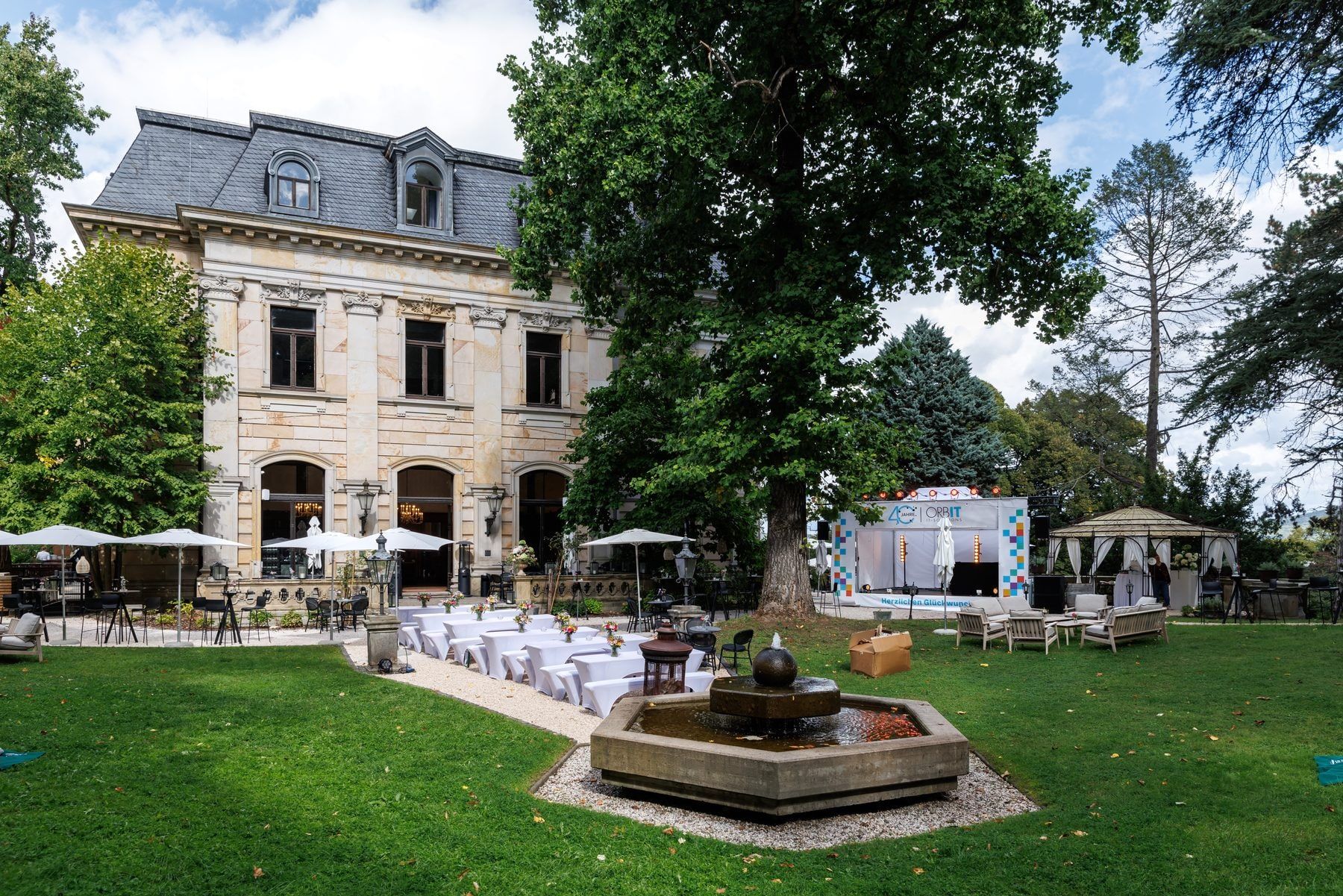 Sommerfest eines Unternehmens im Park der Stella Rheni mit Brunnen, Tafeln und Schirmen vor der Villa