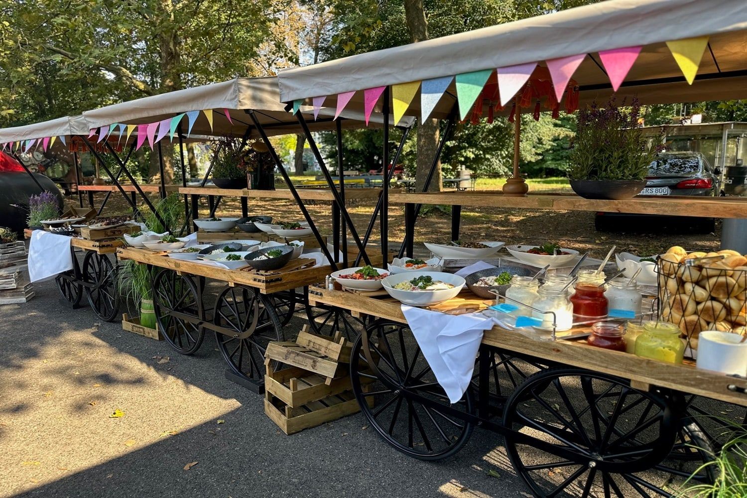 Buffet auf hölzernen Marktkarren unter bunten Wimpelketten auf dem Außengelände des BaseCamp Bonn