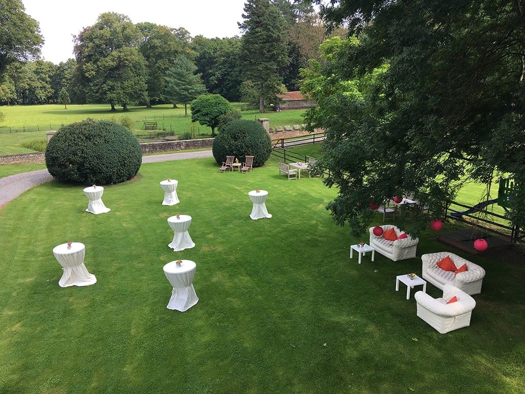 Empfang im Schlosspark von Wachendorf mit weißen Stehtischen, Loungemöbeln und alten Bäumen, von oben aus dem Schloss gesehen