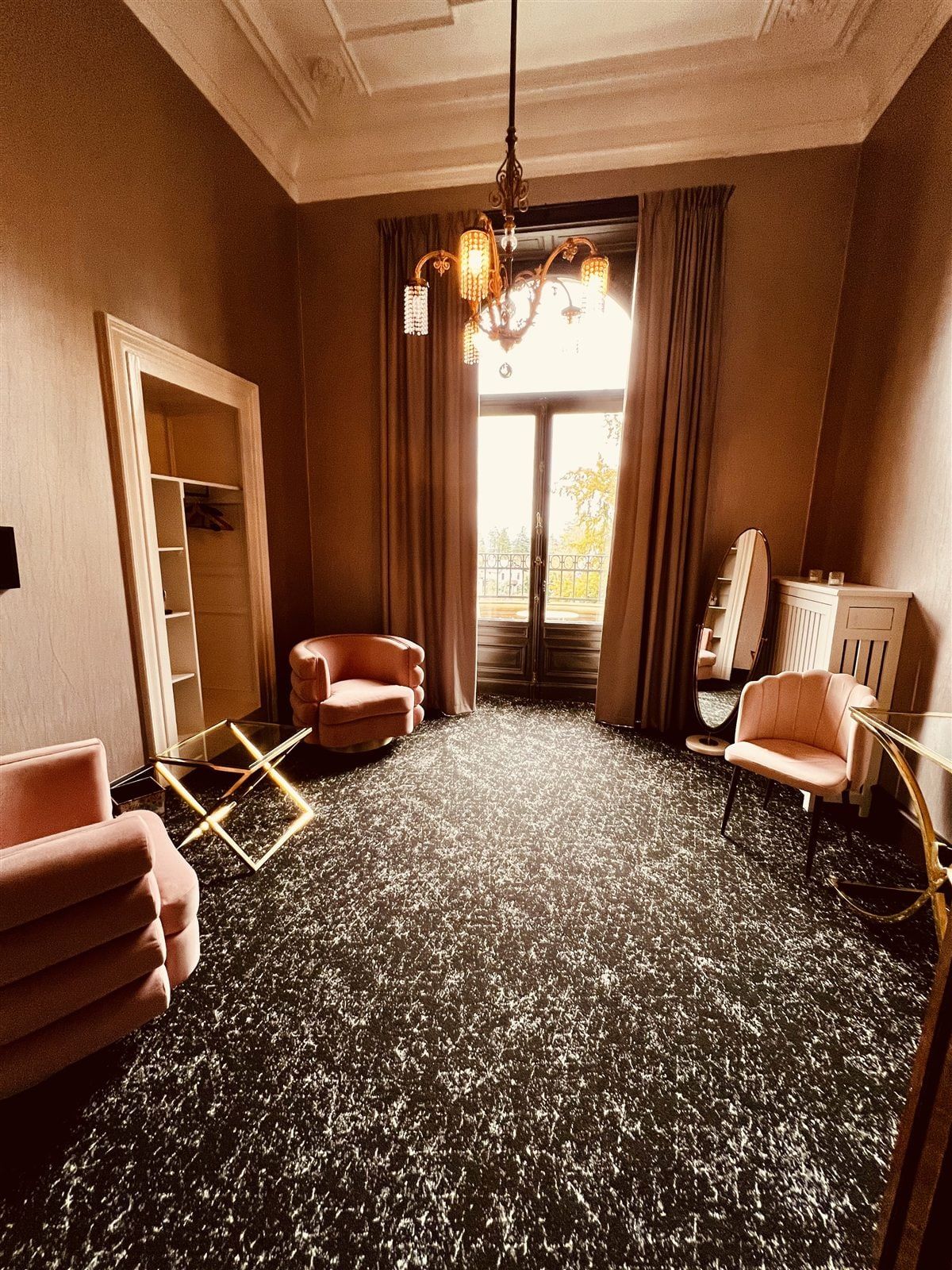 Ein Boutique-Zimmer der Stella Rheni mit Sesseln in Rosé, schweren Vorhängen und Balkontür ins Grüne