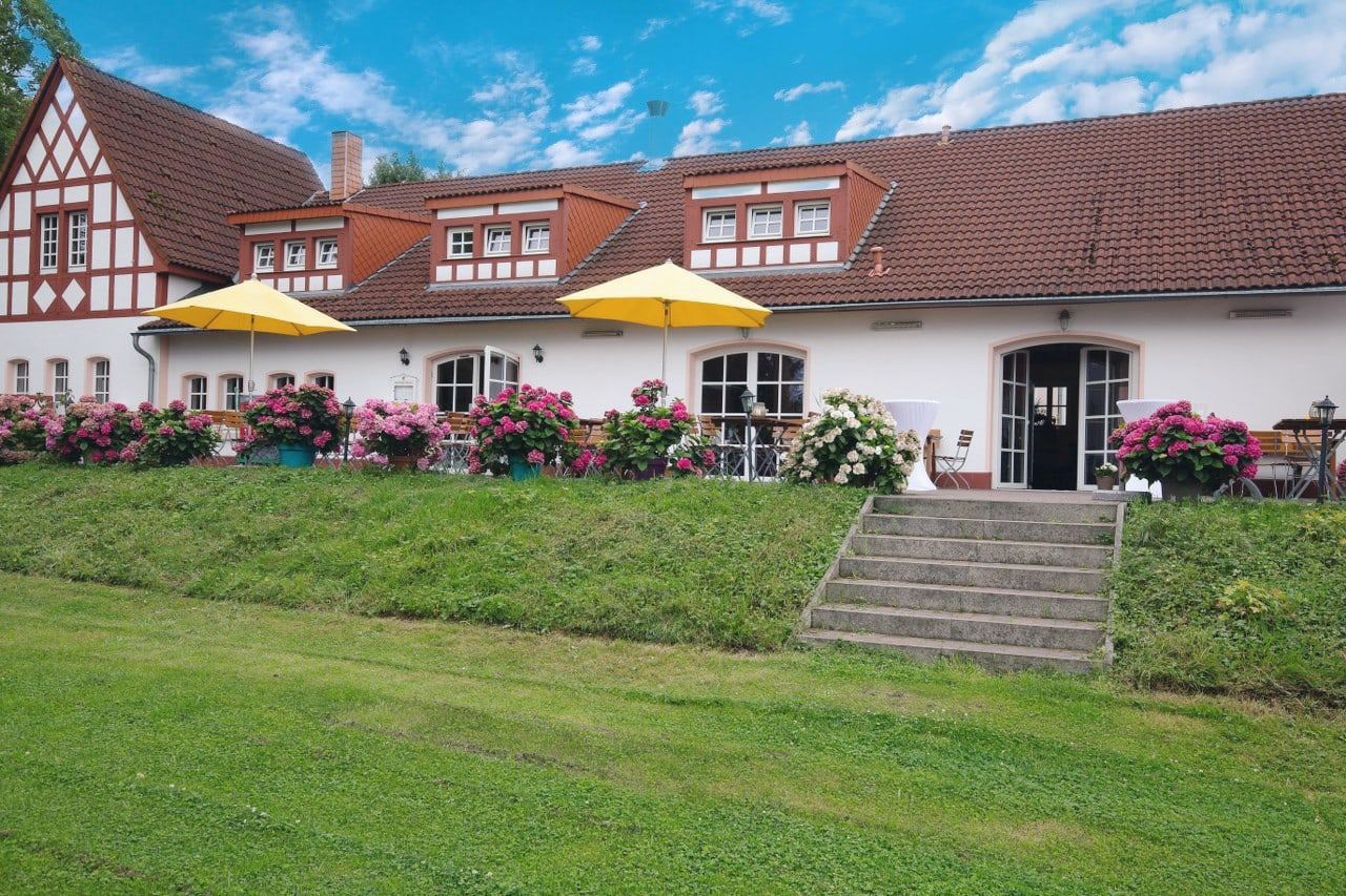 Außenansicht des Weilerhofs in Hürth mit Fachwerkgiebeln, gelben Schirmen und blühenden Hortensien