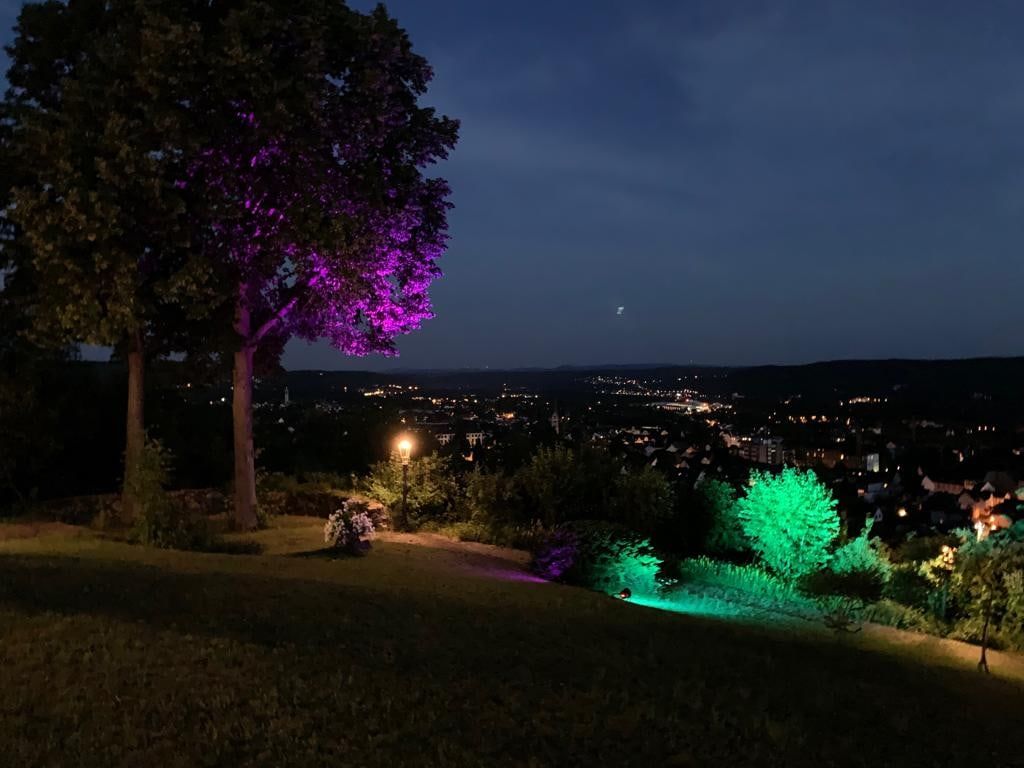 Farbig beleuchtete Bäume im nächtlichen Garten der Villa Heckenfels, darunter die Lichter von Bad Honnef im Tal