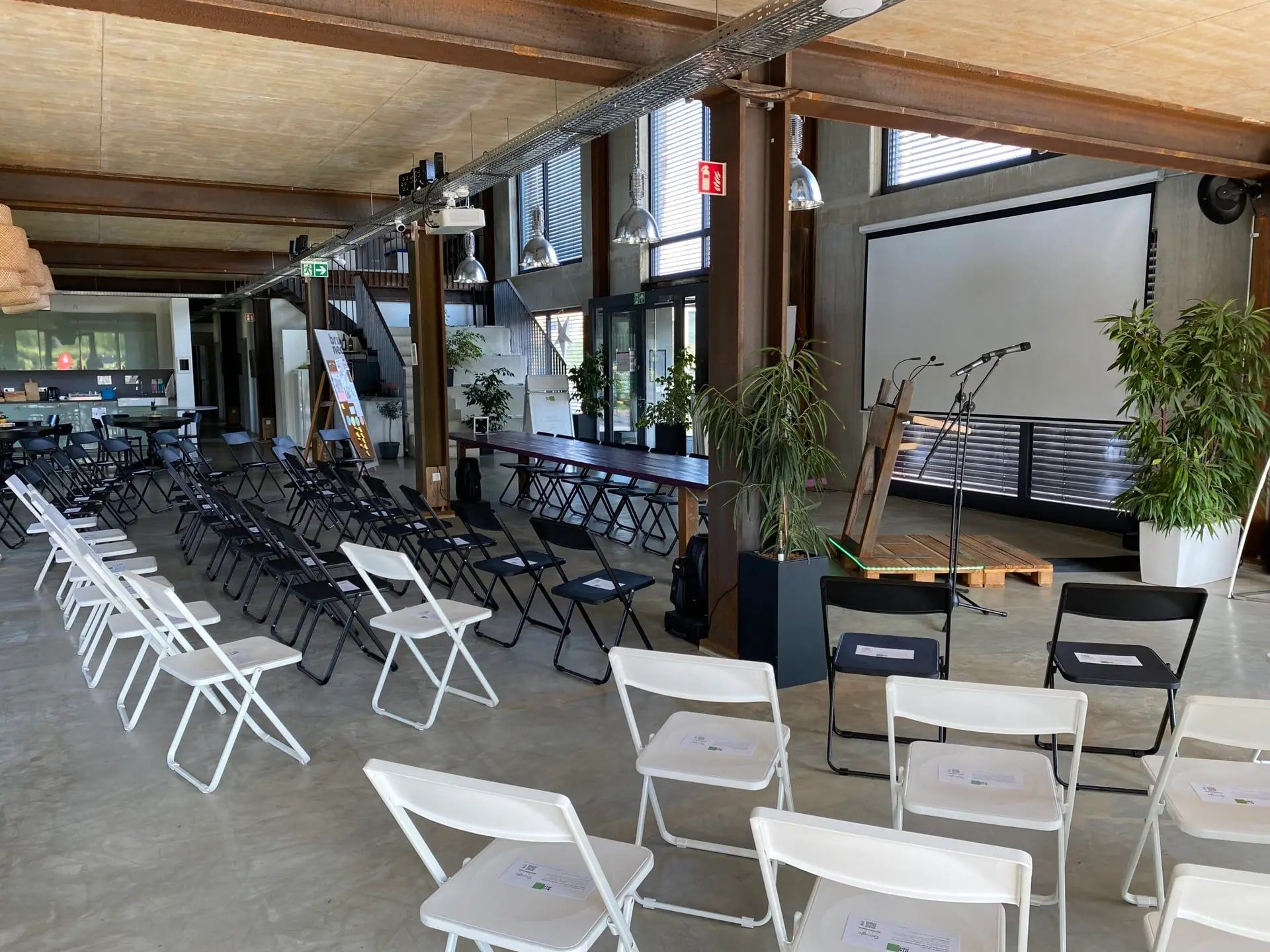 Tagungsraum im Loft des BRÜNEO in Brühl mit Leinwand, Rednerpult, Pflanzen und weißen und schwarzen Stuhlreihen