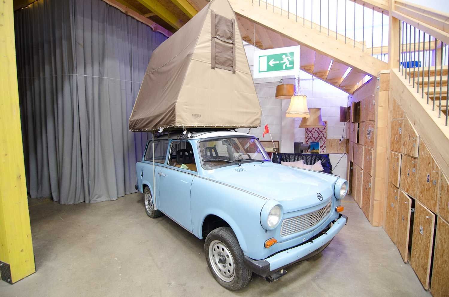 Hellblauer Trabant mit Dachzelt neben einer Holztreppe zur Empore in der Halle des BaseCamp
