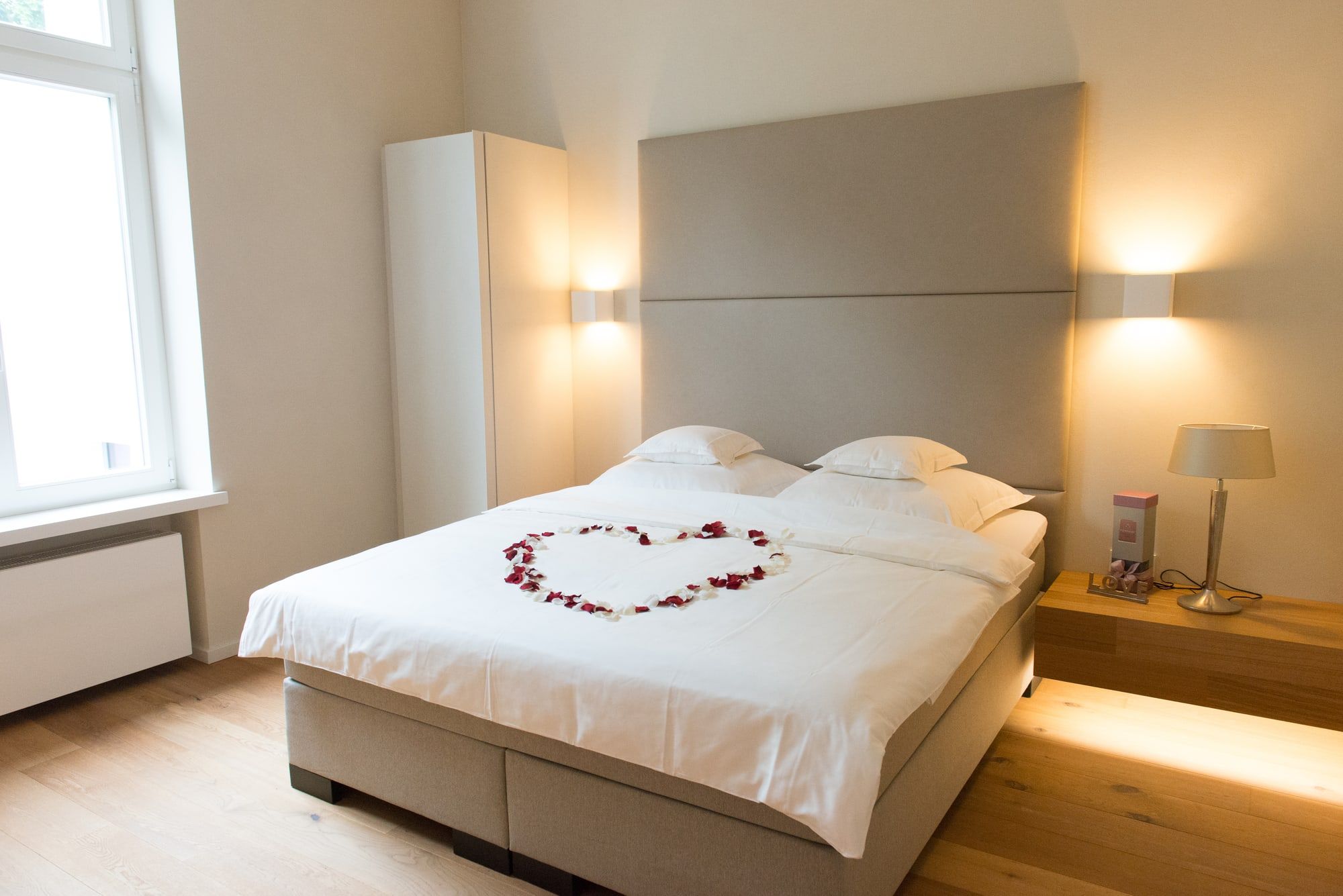 Gästezimmer im Andreashaus mit großem Bett, Rosenblüten in Herzform, warmem Wandlicht und Holzboden