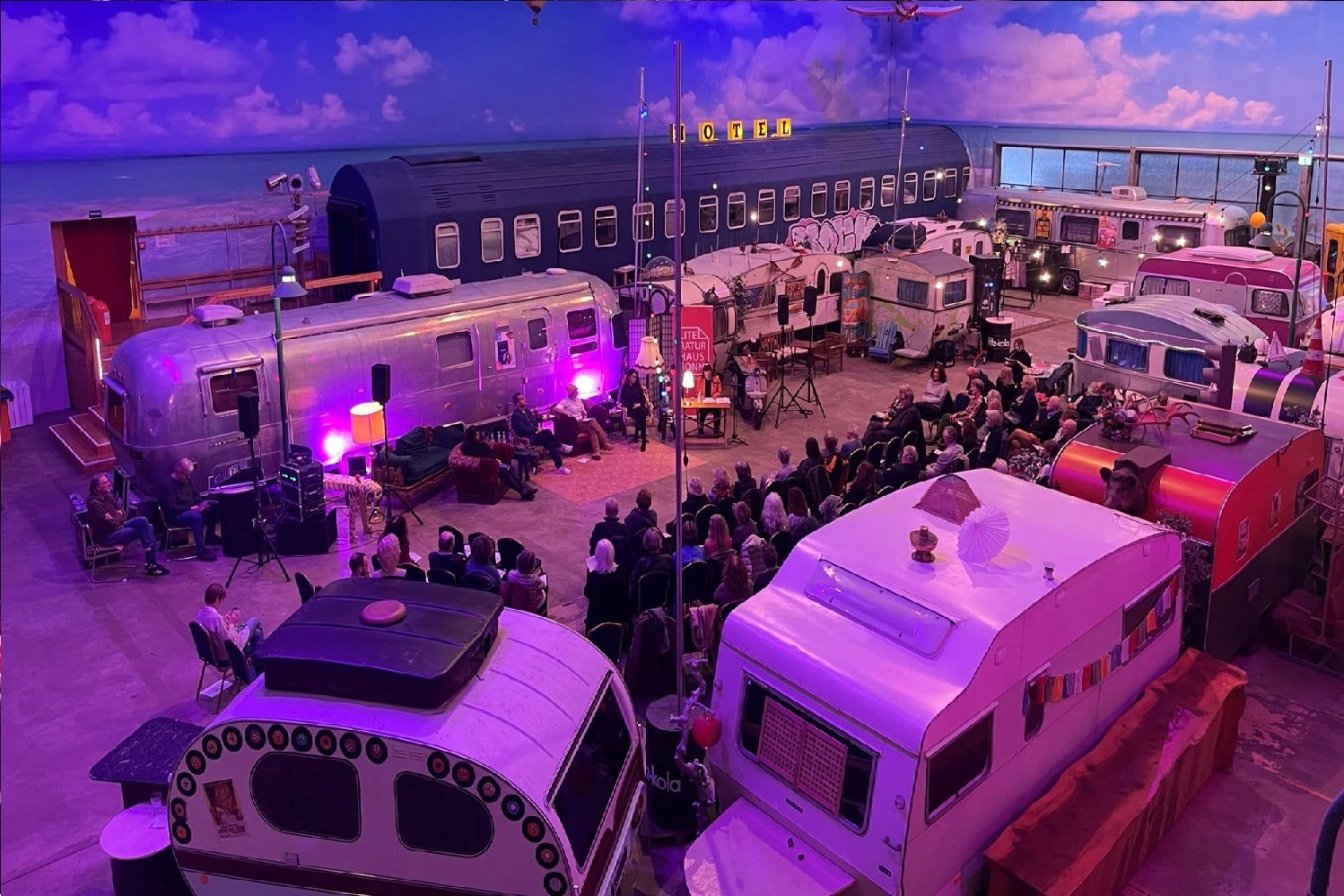 Gäste vor einer Bühne zwischen beleuchteten Wohnwagen bei einer Abendveranstaltung im BaseCamp Bonn