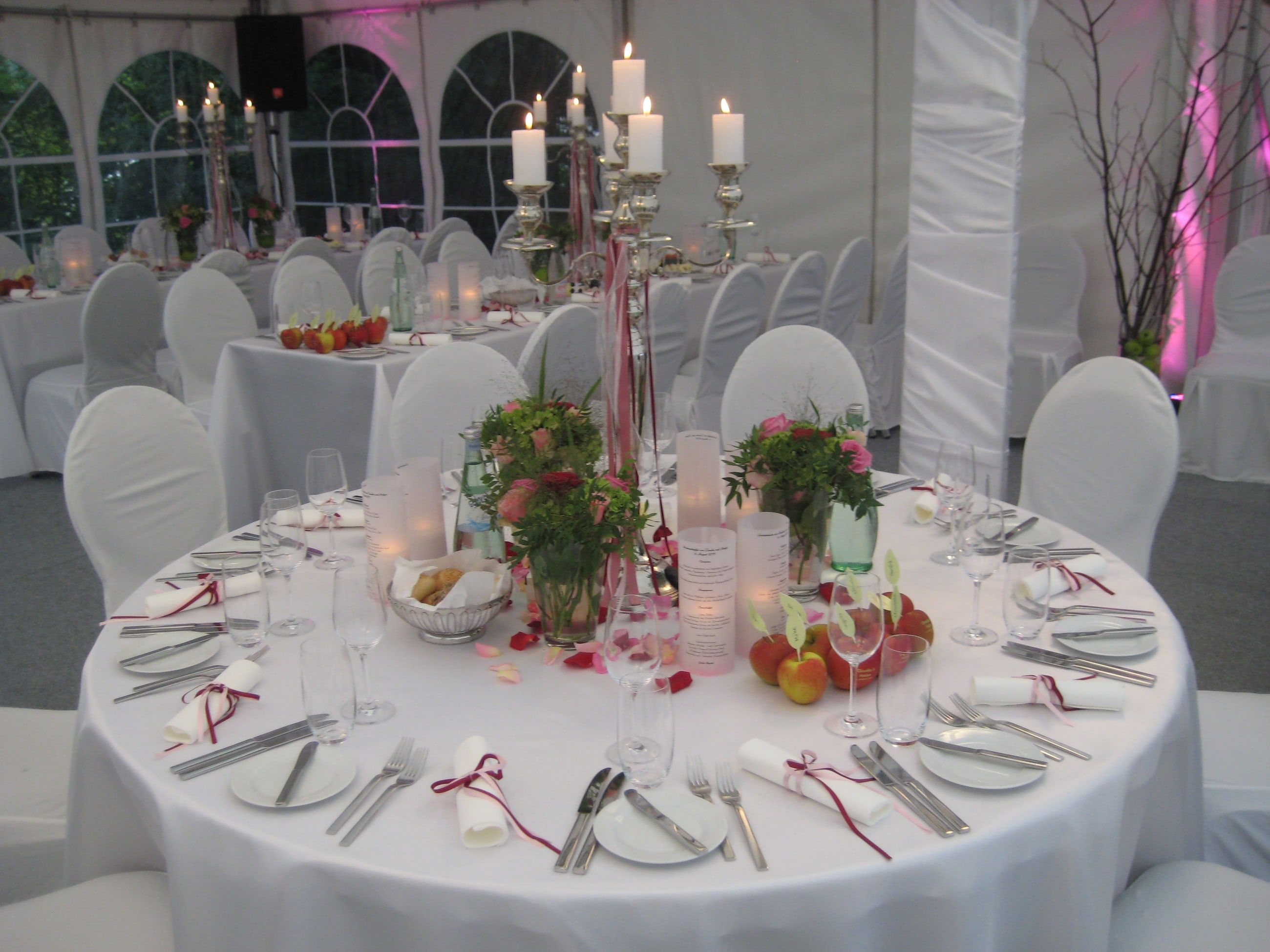 Festlich gedeckte runde Hochzeitstafel in einem Festzelt mit silbernem Kerzenleuchter, Rosen und weißen Hussen